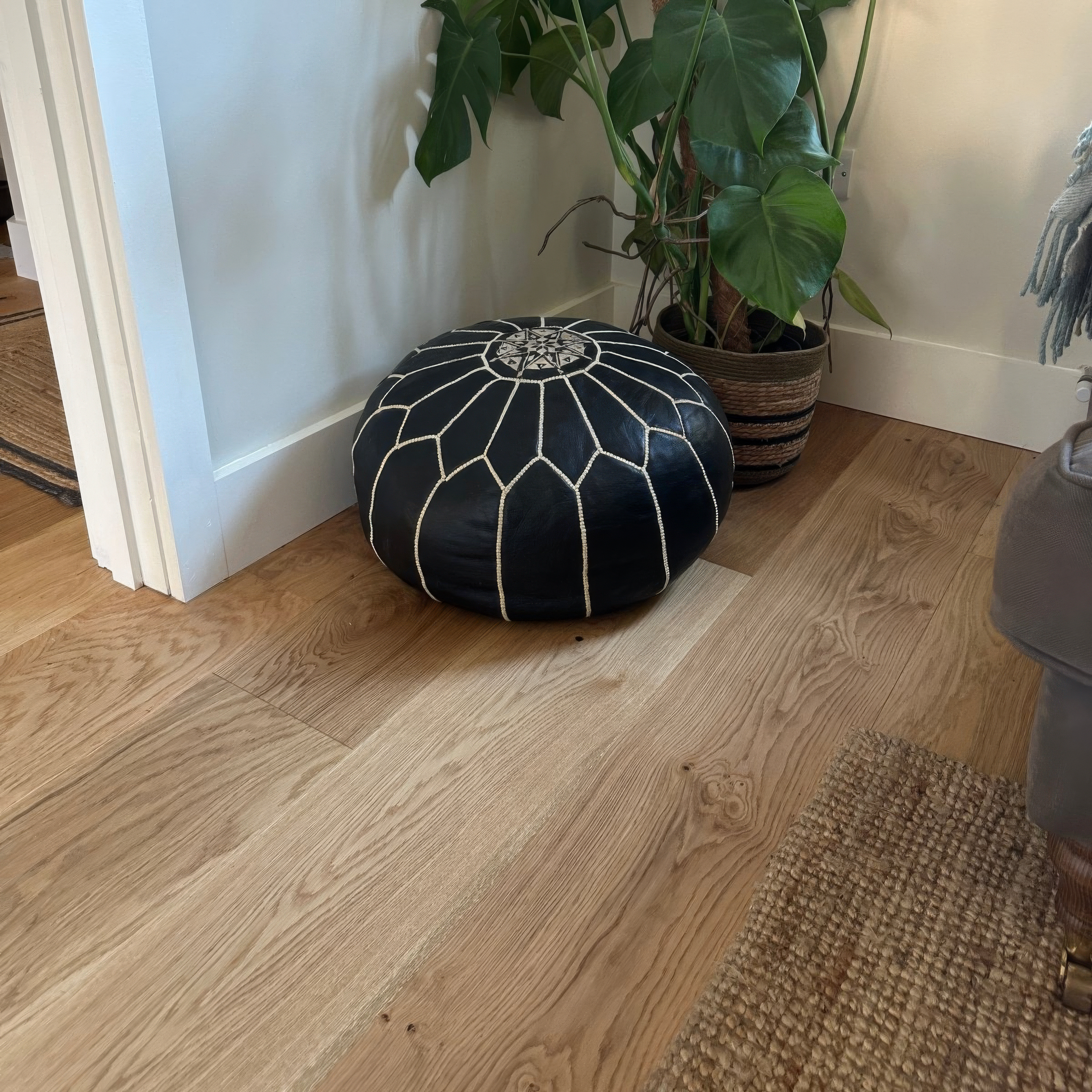 Black patterned ottoman on a wooden floor with a plant in the background