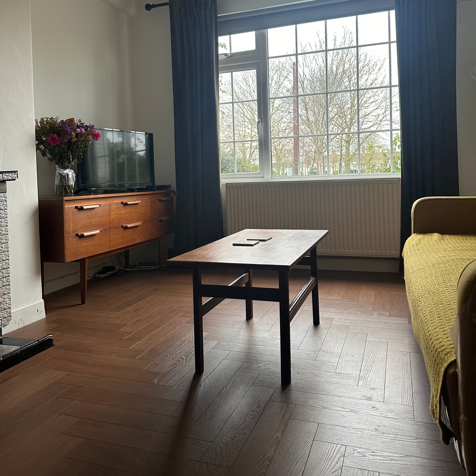 Interior setting showing laminate flooring in a herringbone pattern, with a table, chair, and television visible.