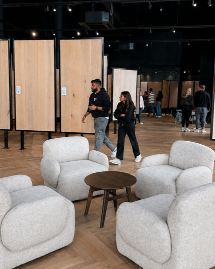 People walking around a room with light gray armchairs and wooden panels.