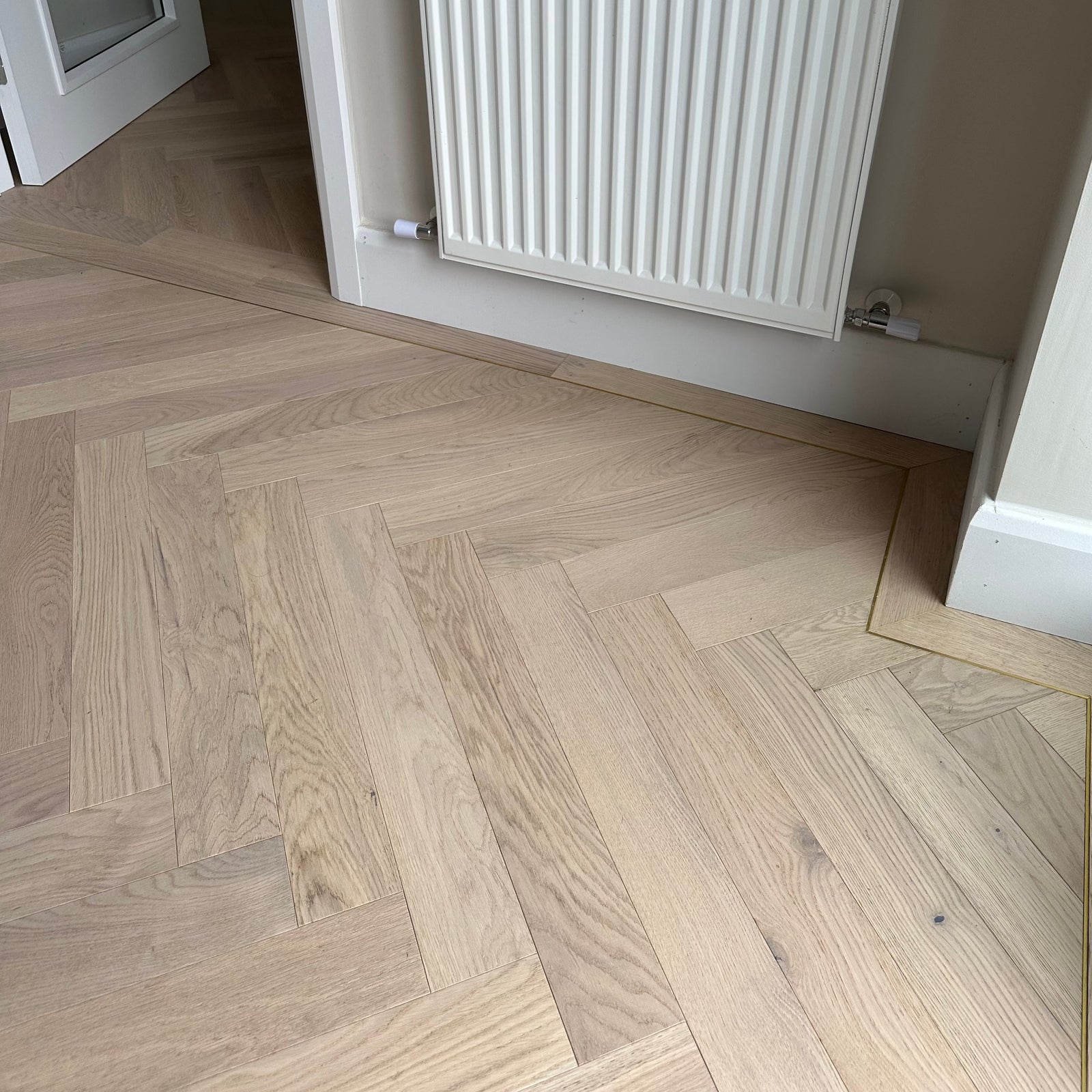 Herringbone patterned wood flooring installed in a room with underfloor heating.