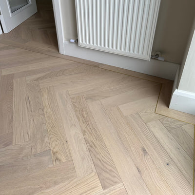 Herringbone patterned wood flooring installed in a room with underfloor heating.